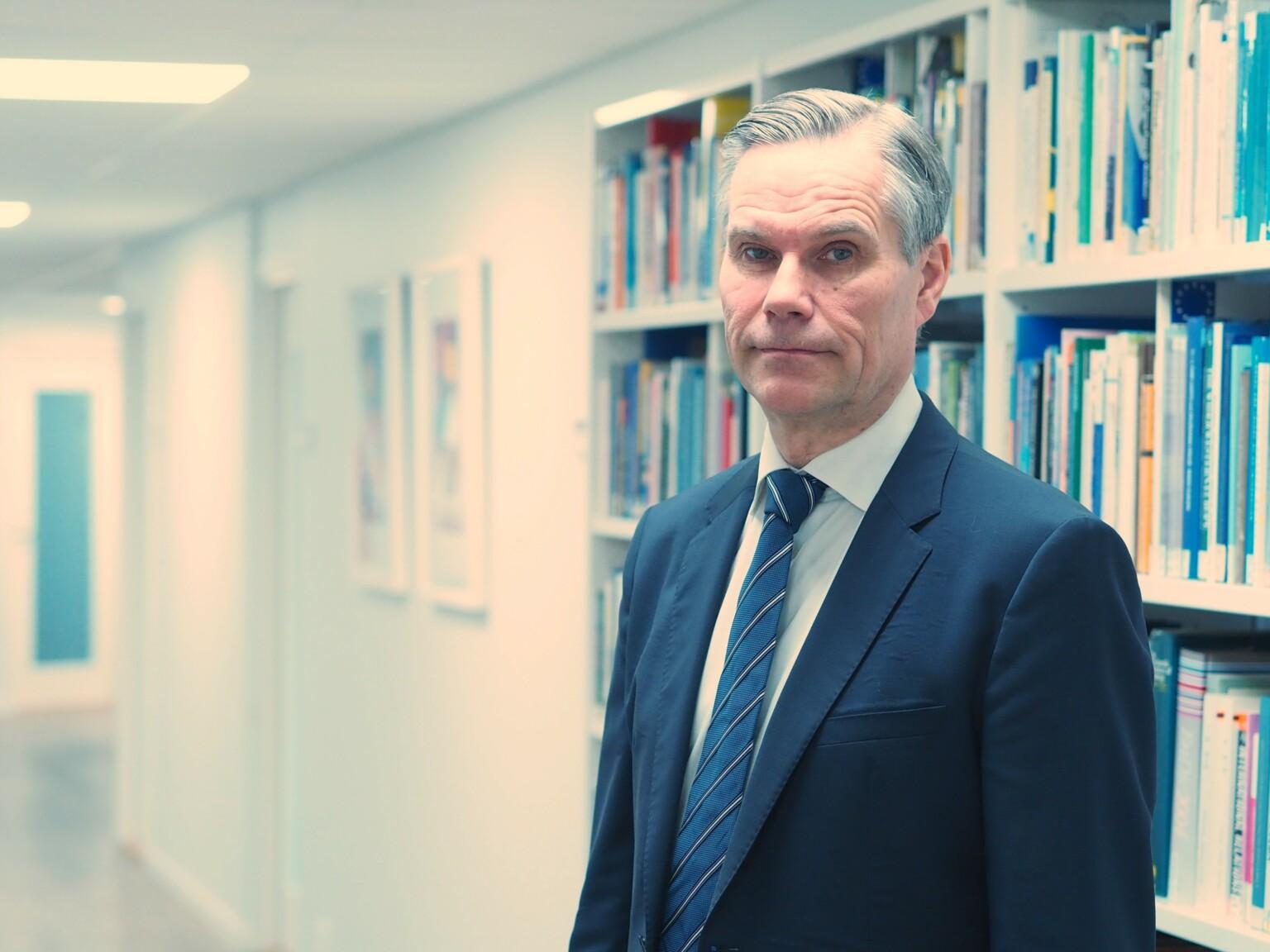 Ambassador Klaus Korhonen infront of a book shelf.