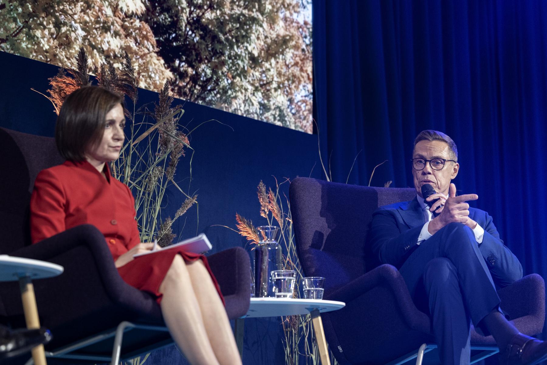 Presidents Maia Sandu and Alexander Stubb on a stage with President Stubb speaking into a microphone.