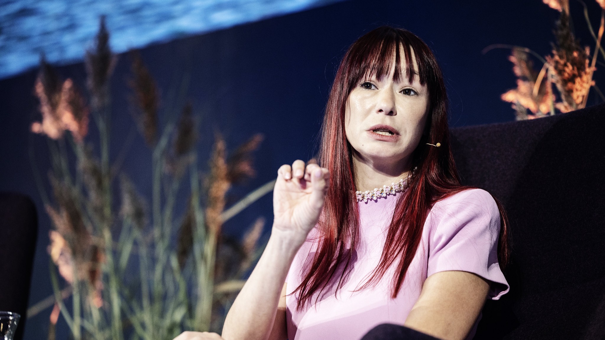 A speaker in a pink dress seated and speaking on the stage.
