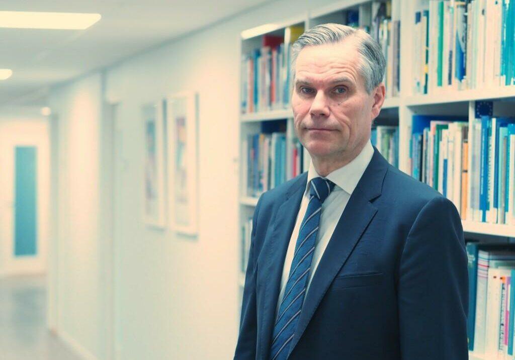 Ambassador Klaus Korhonen infront of a book shelf.